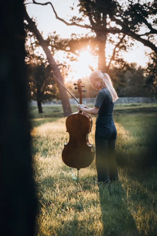 Cellistin Claudia Micheel, die ein Cello hält, vor einem Sonnenuntergang