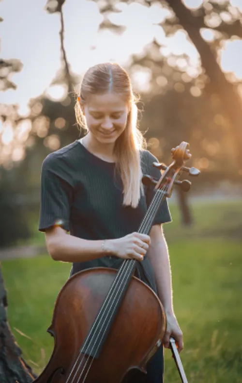 Cellistin Claudia Micheel, die ein Cello hält, vor einem Sonnenuntergang