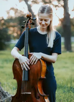 Claudia Micheel mit einem Cello in der Hand vor einem Sonnenuntergang